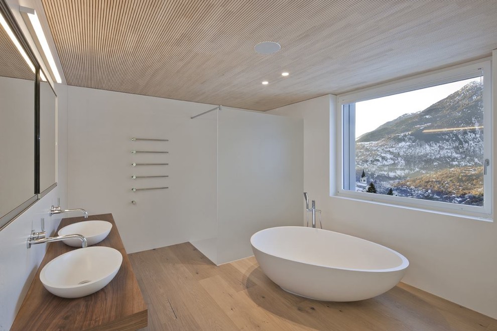Пример оригинального дизайна: главная ванная комната среднего размера в современном стиле с отдельно стоящей ванной, душем без бортиков, белыми стенами, светлым паркетным полом, настольной раковиной, столешницей из дерева, открытым душем и коричневой столешницей