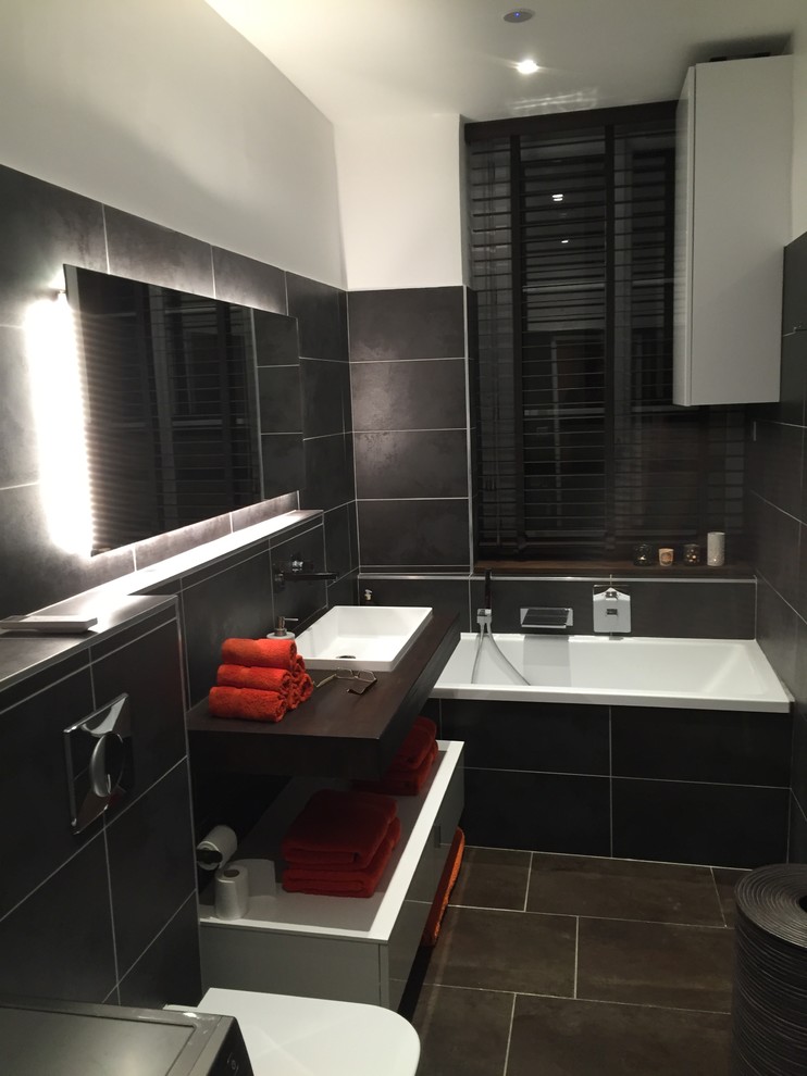 Inredning av ett modernt en-suite badrum, med ett undermonterat badkar, en vägghängd toalettstol, svart kakel, bruna väggar, ett undermonterad handfat och träbänkskiva