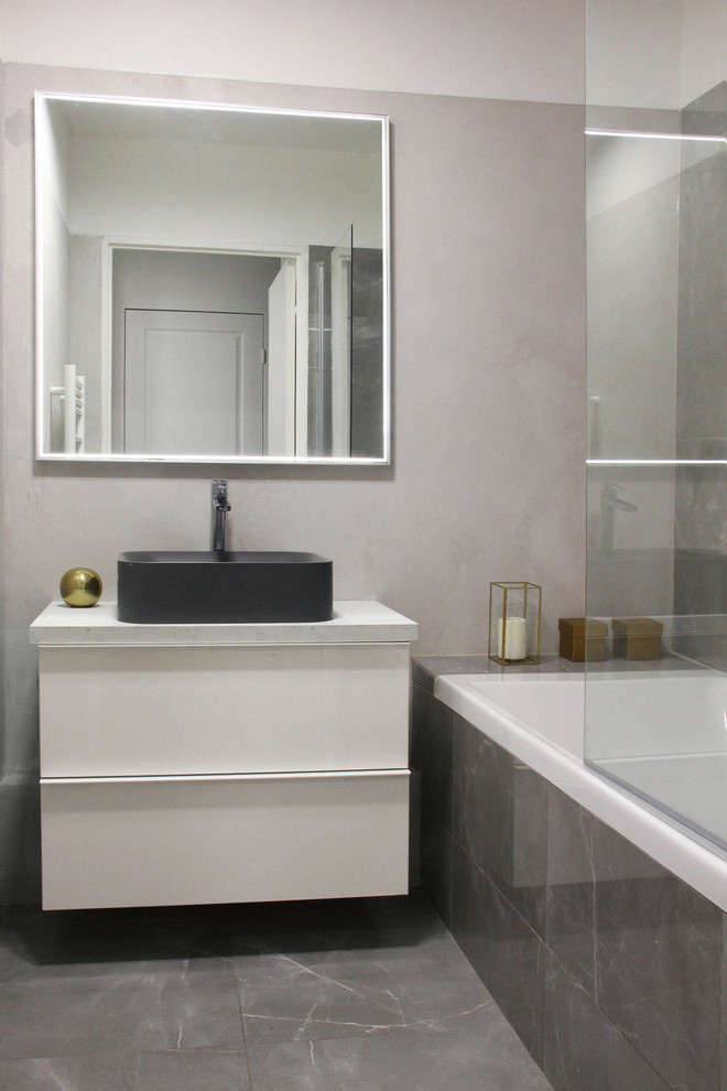 Foto di una piccola stanza da bagno padronale contemporanea con vasca sottopiano, vasca/doccia, piastrelle grigie, pareti grigie, pavimento in marmo, lavabo a consolle e top piastrellato