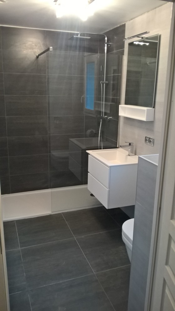 Exempel på ett litet modernt vit vitt badrum med dusch, med släta luckor, vita skåp, en kantlös dusch, en vägghängd toalettstol, grå kakel, keramikplattor, grå väggar, klinkergolv i keramik, ett väggmonterat handfat, svart golv och med dusch som är öppen