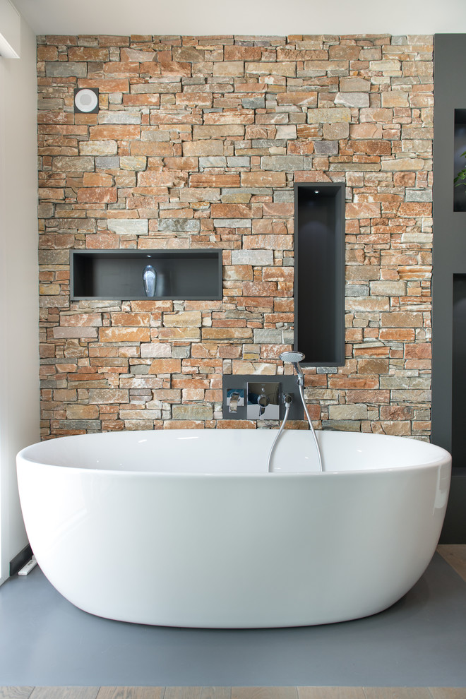 Cette image montre une salle de bain principale design avec une baignoire indépendante, un carrelage de pierre et un mur en pierre.