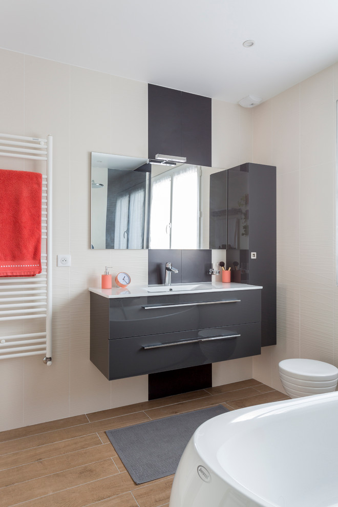 Foto de cuarto de baño principal y gris y blanco actual de tamaño medio con bañera exenta, puertas de armario grises, paredes blancas, suelo de madera en tonos medios y lavabo integrado