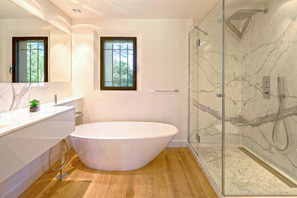 Modern inredning av ett en-suite badrum, med vita skåp, ett platsbyggt badkar, en hörndusch, vita väggar, ljust trägolv, ett integrerad handfat och marmorbänkskiva