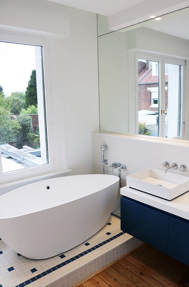 Photo of a small modern shower room bathroom in Lille with blue cabinets, a built-in bath, a walk-in shower, a wall mounted toilet, white tiles, ceramic tiles, blue walls, light hardwood flooring, a vessel sink, wooden worktops, beige floors, an open shower and blue worktops.