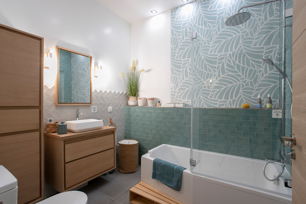 Inspiration för mellanstora minimalistiska brunt en-suite badrum, med skåp i ljust trä, travertinkakel, vita väggar, träbänkskiva, grått golv, luckor med profilerade fronter, ett platsbyggt badkar, en dusch/badkar-kombination, en vägghängd toalettstol, grön kakel, cementgolv, ett fristående handfat och dusch med gångjärnsdörr