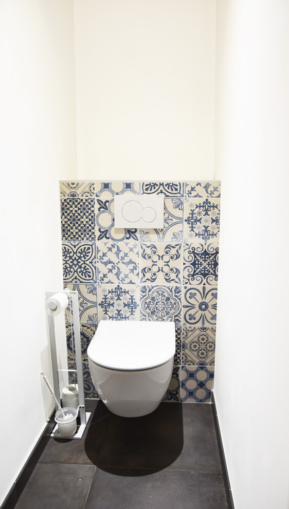 Modern inredning av ett mellanstort toalett, med luckor med profilerade fronter, vita skåp, cementkakel, vita väggar, ett undermonterad handfat, grått golv, flerfärgad kakel, klinkergolv i keramik och laminatbänkskiva