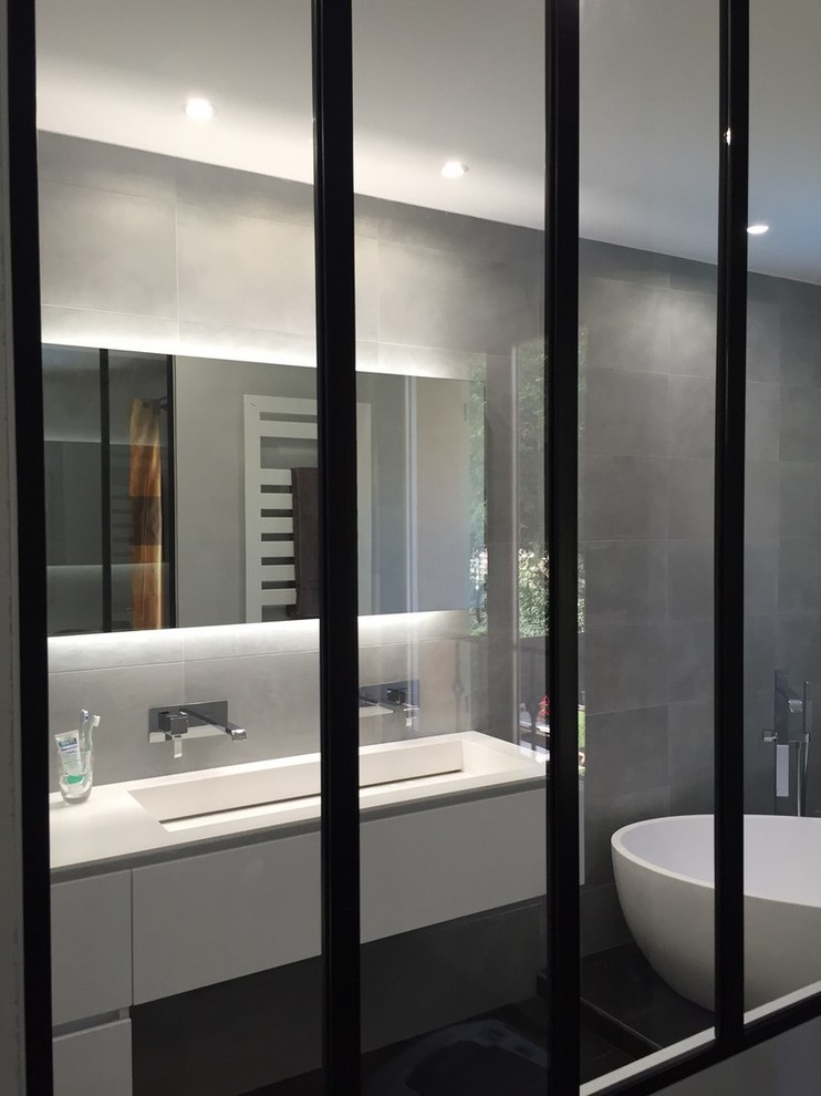 Modern inredning av ett mellanstort en-suite badrum, med vita skåp, ett platsbyggt badkar, grå kakel, keramikplattor, grå väggar, cementgolv, ett konsol handfat, bänkskiva i akrylsten och svart golv