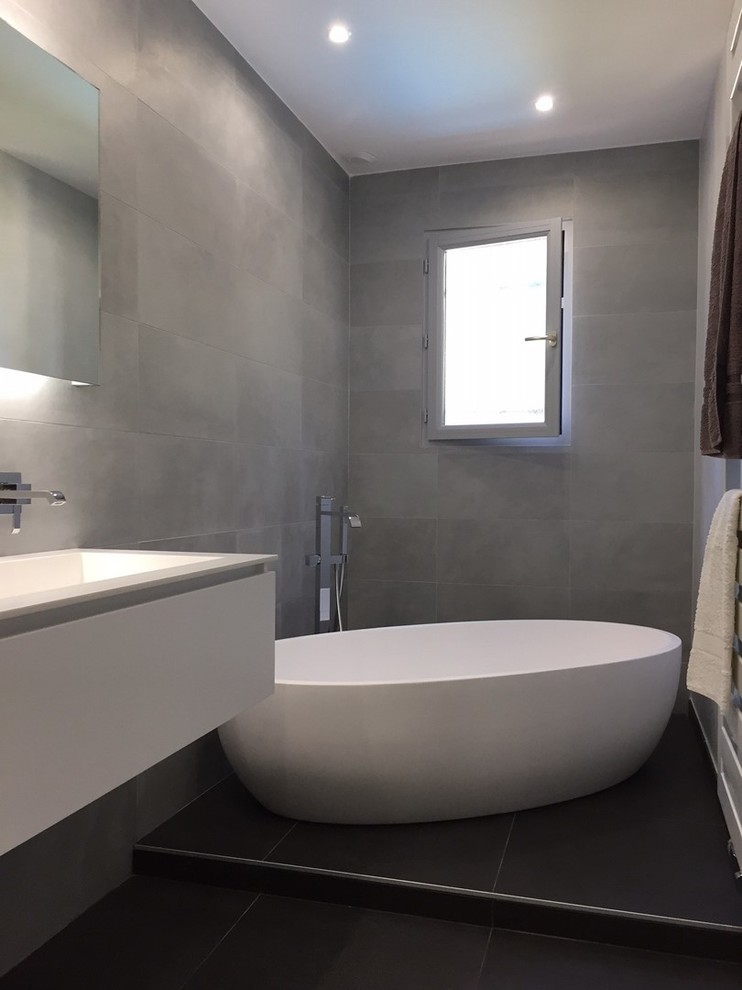 This is an example of a medium sized contemporary ensuite bathroom in Lyon with white cabinets, a built-in bath, grey tiles, ceramic tiles, grey walls, cement flooring, a console sink, solid surface worktops and black floors.