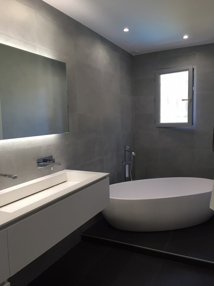 Photo of a medium sized contemporary ensuite bathroom in Lyon with white cabinets, a built-in bath, grey tiles, ceramic tiles, grey walls, cement flooring, a console sink, solid surface worktops and black floors.