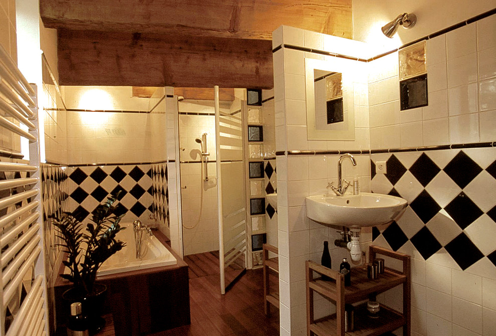 60 tals inredning av ett stort en-suite badrum, med ett väggmonterat handfat, en jacuzzi, en kantlös dusch, en toalettstol med hel cisternkåpa, svart och vit kakel, porslinskakel, vita väggar och mellanmörkt trägolv