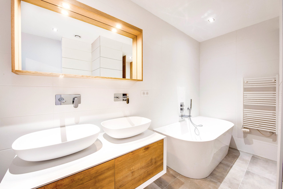 Пример оригинального дизайна: главная ванная комната в современном стиле с плоскими фасадами, фасадами цвета дерева среднего тона, отдельно стоящей ванной, белыми стенами, настольной раковиной, серым полом и белой столешницей