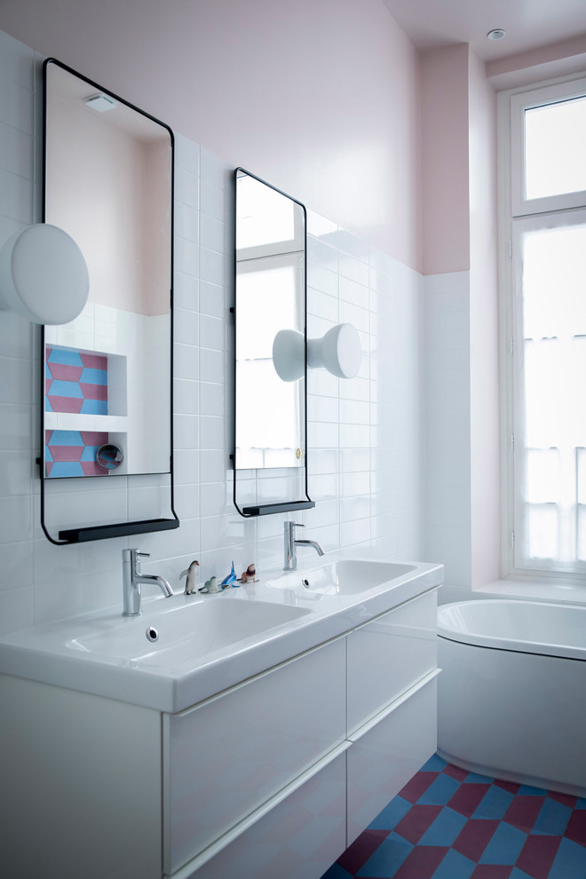 Modern inredning av ett badrum, med släta luckor, vita skåp, ett fristående badkar, vit kakel, rosa väggar, ett konsol handfat och flerfärgat golv