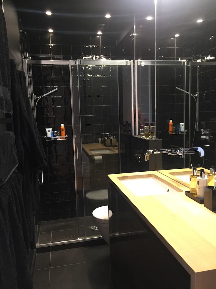 Foto på ett litet funkis en-suite badrum, med släta luckor, svarta skåp, en kantlös dusch, en vägghängd toalettstol, svart kakel, perrakottakakel, svarta väggar, klinkergolv i keramik, ett undermonterad handfat och träbänkskiva