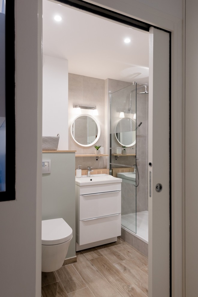 Cette image montre une salle de bain design avec un placard à porte plane, des portes de placard blanches, WC suspendus, un carrelage gris, un mur blanc, parquet clair, un plan vasque, un sol beige et aucune cabine.