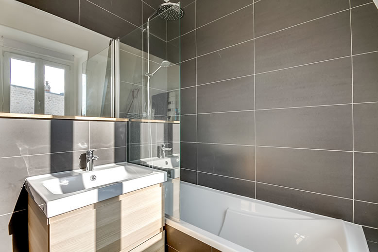 Réalisation d'une petite salle de bain principale design en bois clair avec une baignoire encastrée, WC suspendus, un carrelage gris, des carreaux de céramique, un mur gris, parquet clair, un plan vasque et un plan de toilette en surface solide.