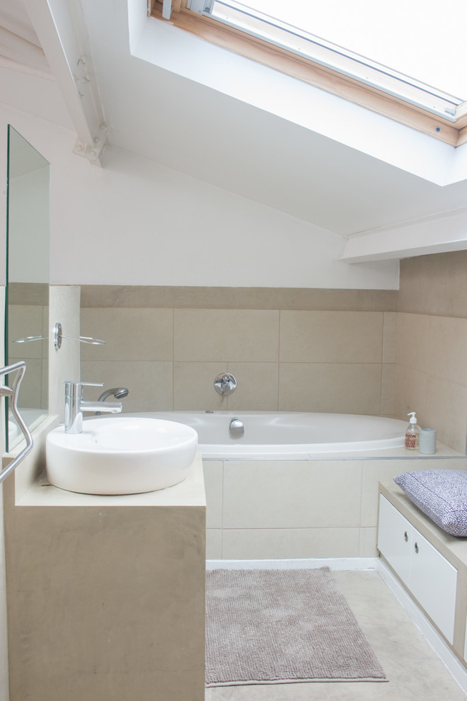 Cette image montre une salle de bain principale design de taille moyenne avec des portes de placard blanches, une baignoire posée, un carrelage beige, un mur blanc et une vasque.