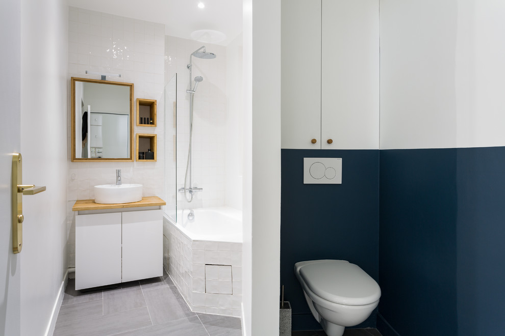Foto på ett litet skandinaviskt beige en-suite badrum, med släta luckor, vita skåp, ett undermonterat badkar, en vägghängd toalettstol, vit kakel, keramikplattor, ett nedsänkt handfat och träbänkskiva