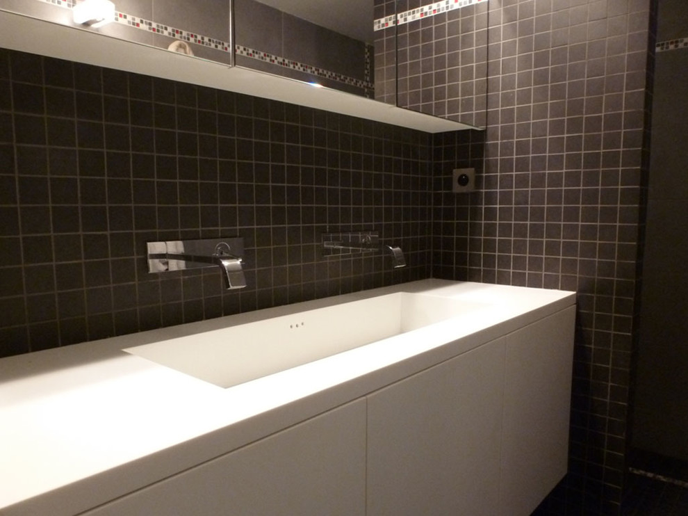 Bild på ett mellanstort funkis vit vitt badrum med dusch, med luckor med profilerade fronter, vita skåp, en kantlös dusch, en toalettstol med separat cisternkåpa, svart kakel, mosaik, svarta väggar, klinkergolv i keramik, ett integrerad handfat, bänkskiva i akrylsten, grått golv och med dusch som är öppen