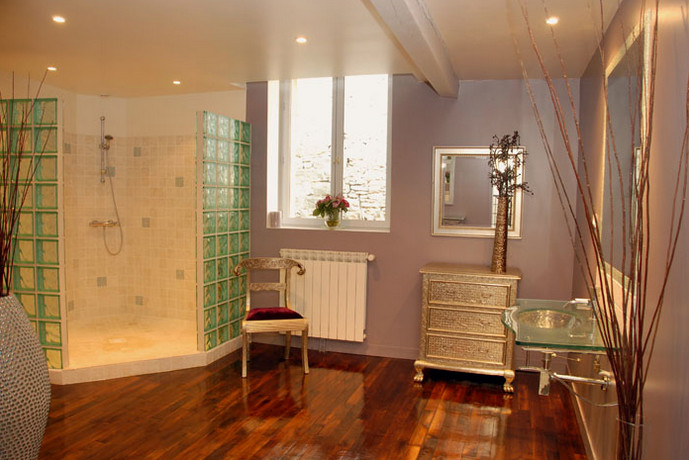 Cette photo montre une grande salle de bain principale romantique avec une douche à l'italienne, WC suspendus, un carrelage beige, un carrelage de pierre, un mur violet, parquet foncé, un lavabo intégré, un plan de toilette en verre, un sol marron et aucune cabine.