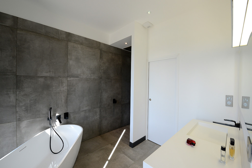 Idées déco pour une grande salle de bain principale contemporaine avec une baignoire posée, un carrelage gris, des carreaux de céramique, un mur blanc, un sol en carrelage de céramique, un lavabo suspendu, un plan de toilette en surface solide, un sol gris et un plan de toilette blanc.