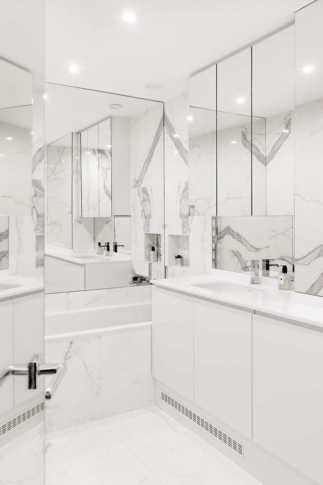 Inspiration pour une salle de bain principale design de taille moyenne avec un placard à porte affleurante, des portes de placard blanches, une baignoire encastrée, un espace douche bain, WC suspendus, un carrelage blanc, du carrelage en marbre, un mur blanc, un sol en marbre, un lavabo encastré, un plan de toilette en quartz et un sol blanc.
