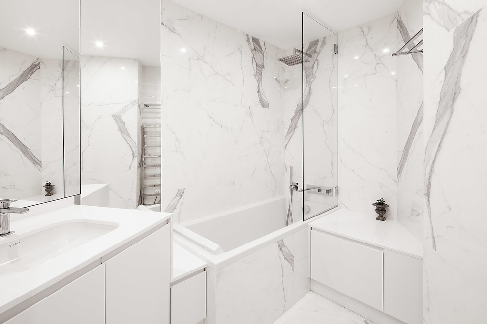 Inspiration pour une salle de bain principale design de taille moyenne avec un placard à porte affleurante, des portes de placard blanches, une baignoire encastrée, un espace douche bain, WC suspendus, un carrelage blanc, du carrelage en marbre, un mur blanc, un sol en marbre, un lavabo encastré, un plan de toilette en quartz et un sol blanc.
