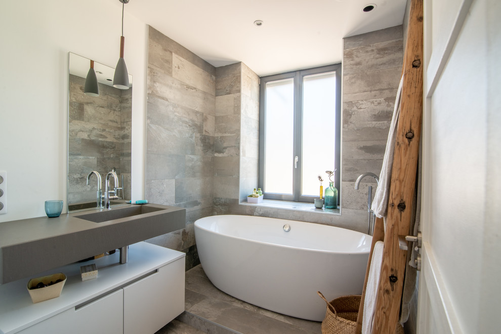 Foto på ett funkis grå badrum med dusch, med släta luckor, vita skåp, ett fristående badkar, grå kakel, vita väggar, ett integrerad handfat och grått golv