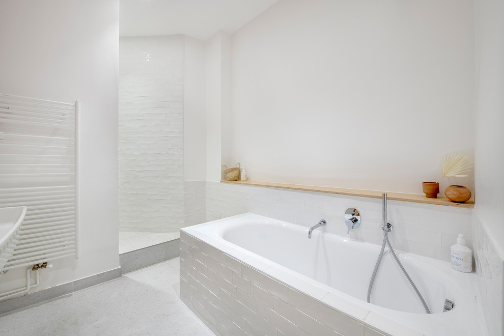 パリにあるお手頃価格の広いシャビーシック調のおしゃれなマスターバスルーム (オープンシェルフ、白いキャビネット、ドロップイン型浴槽、シャワー付き浴槽	、白いタイル、テラコッタタイル、白い壁、テラゾーの床、横長型シンク、人工大理石カウンター、白い床、オープンシャワー、白い洗面カウンター、洗面台2つ) の写真