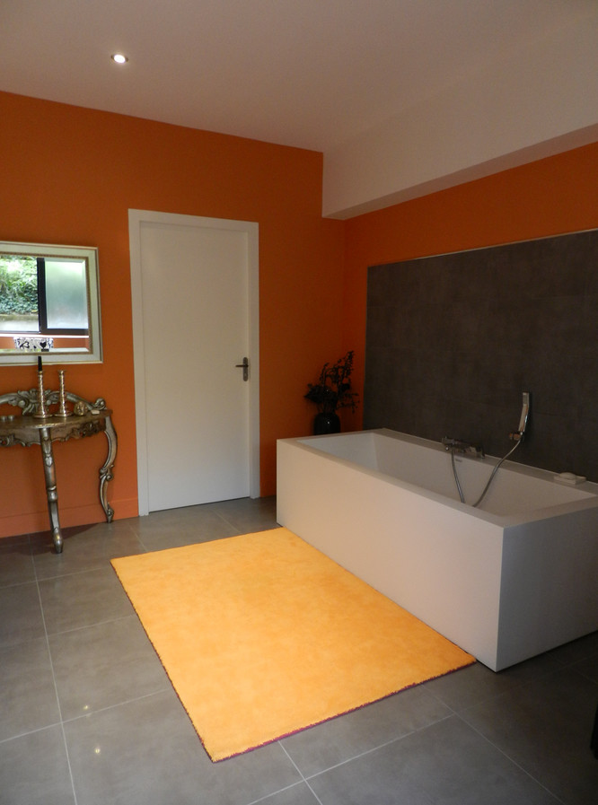 Exemple d'une grande salle de bain principale tendance avec des portes de placard blanches, une baignoire posée, une douche à l'italienne, des carreaux de céramique, un mur orange, un sol en carrelage de céramique, un lavabo suspendu, un plan de toilette en surface solide, un carrelage noir et un sol gris.