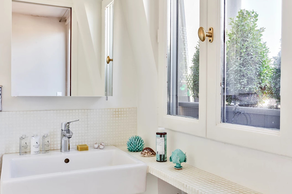 Bild på ett litet funkis vit vitt badrum med dusch, med vita skåp, en kantlös dusch, en vägghängd toalettstol, vit kakel, mosaik, vita väggar, mosaikgolv, ett fristående handfat, kaklad bänkskiva, med dusch som är öppen och vitt golv