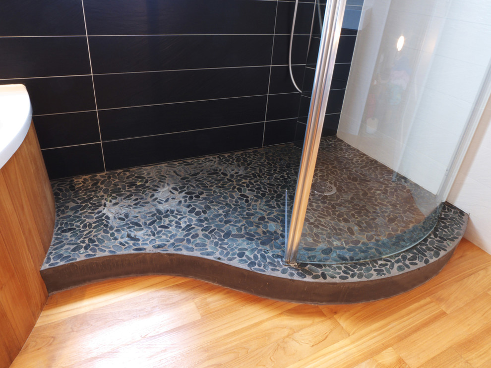 Ejemplo de cuarto de baño actual con baldosas y/o azulejos negros, suelo de baldosas tipo guijarro y ducha con puerta con bisagras