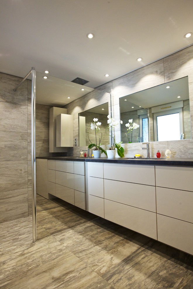 Modelo de cuarto de baño contemporáneo de tamaño medio con aseo y ducha, ducha a ras de suelo, baldosas y/o azulejos grises, paredes grises y lavabo integrado