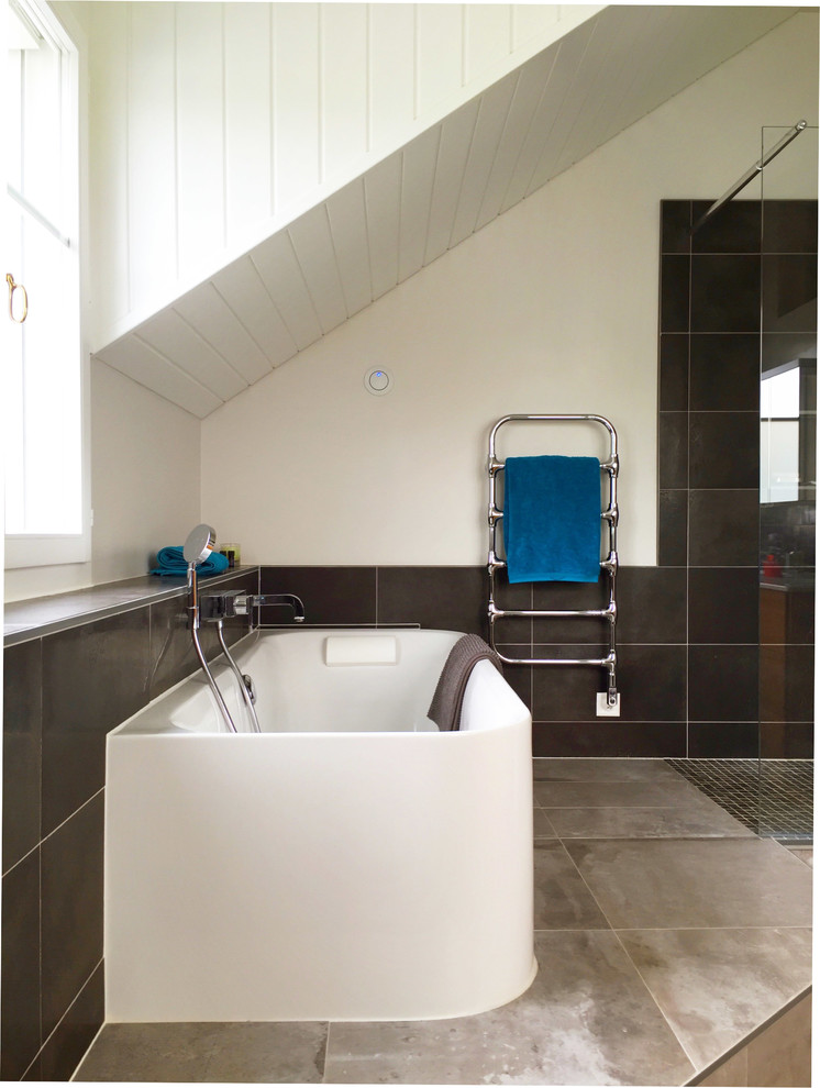 Modern inredning av ett badrum, med ett fristående badkar, en kantlös dusch, en vägghängd toalettstol, porslinskakel, grå väggar, klinkergolv i porslin och ett undermonterad handfat