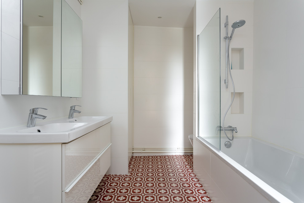 Idéer för att renovera ett mellanstort funkis vit vitt en-suite badrum, med vita skåp, vita väggar, släta luckor, ett platsbyggt badkar, en dusch/badkar-kombination, vit kakel, porslinskakel, cementgolv, ett konsol handfat, bänkskiva i akrylsten, rött golv och dusch med gångjärnsdörr