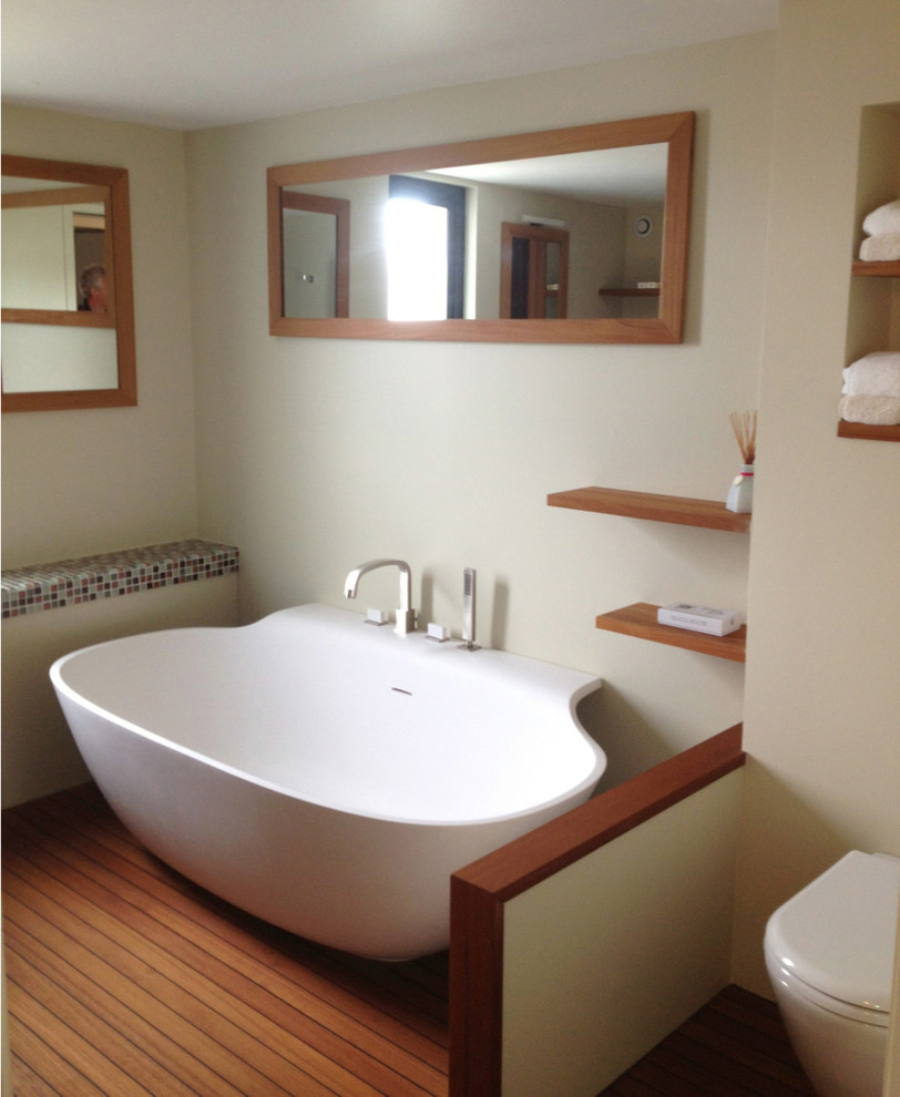 Ejemplo de cuarto de baño actual con bañera exenta, sanitario de pared, suelo de madera clara y lavabo tipo consola