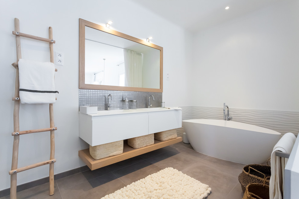 Exemple d'une salle de bain scandinave avec un placard à porte plane, des portes de placard blanches, une baignoire indépendante, un mur blanc, un lavabo encastré et un sol beige.
