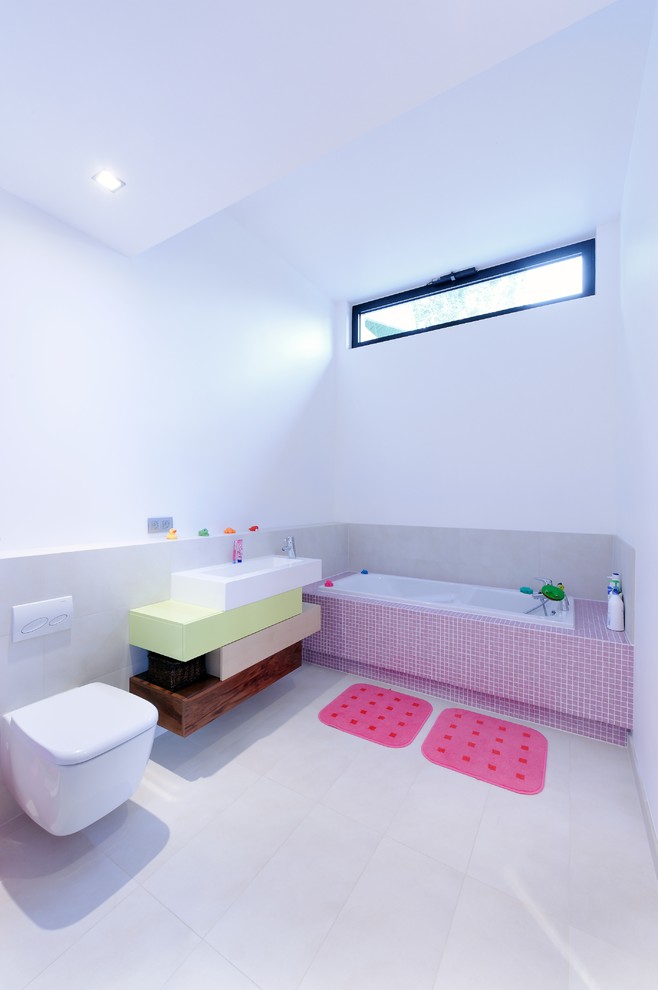 Inspiration pour une salle de bain design de taille moyenne pour enfant avec une baignoire encastrée, WC suspendus, un carrelage gris, un mur blanc, un sol en carrelage de céramique et une vasque.