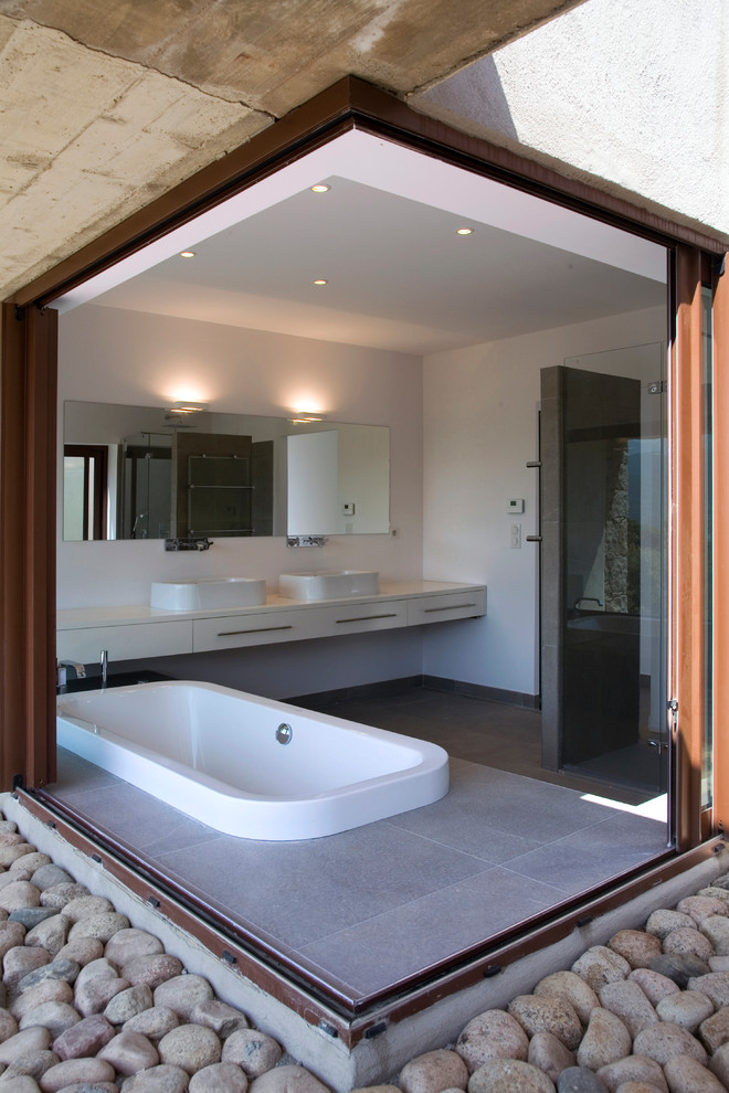 Diseño de cuarto de baño principal actual con lavabo sobreencimera, armarios con paneles lisos, puertas de armario blancas, bañera encastrada y paredes blancas