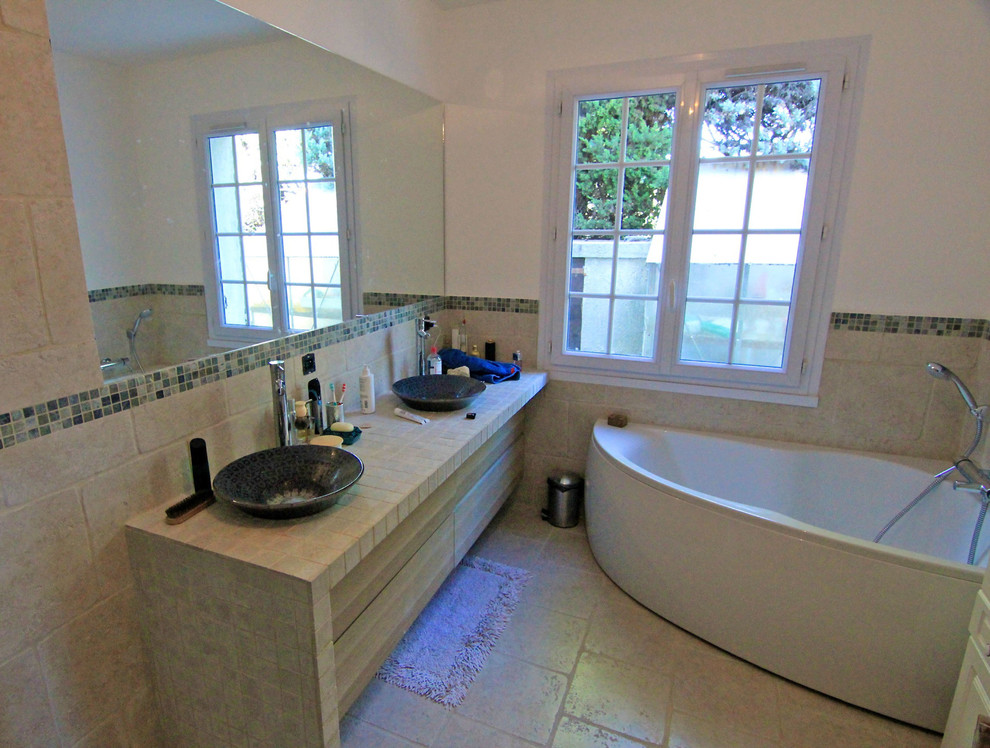 Photo of a large contemporary ensuite bathroom in Marseille with raised-panel cabinets, light wood cabinets, a corner bath, a built-in shower, a wall mounted toilet, beige tiles, stone slabs, white walls, marble flooring, a console sink and limestone worktops.