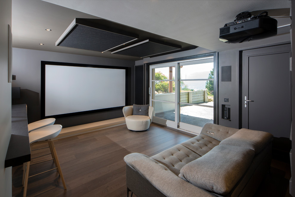Ejemplo de cine en casa abierto contemporáneo pequeño con paredes grises, suelo de madera en tonos medios y pantalla de proyección