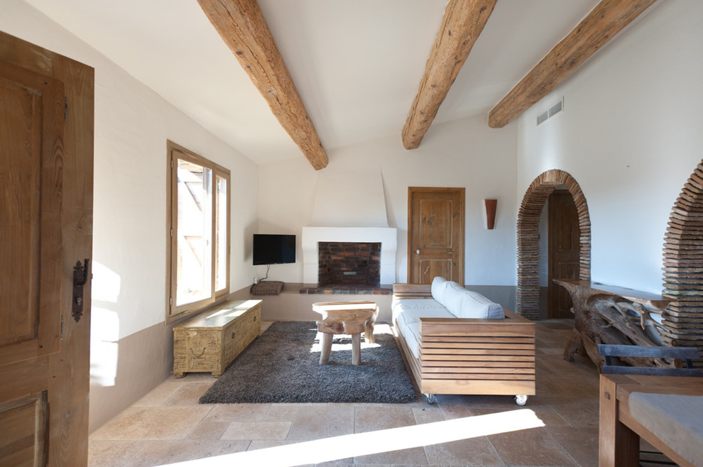 На фото: гостиная комната в средиземноморском стиле с белыми стенами, стандартным камином и телевизором на стене