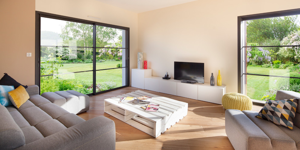 Cette image montre une salle de séjour design avec un mur beige, un sol en bois brun et un téléviseur indépendant.