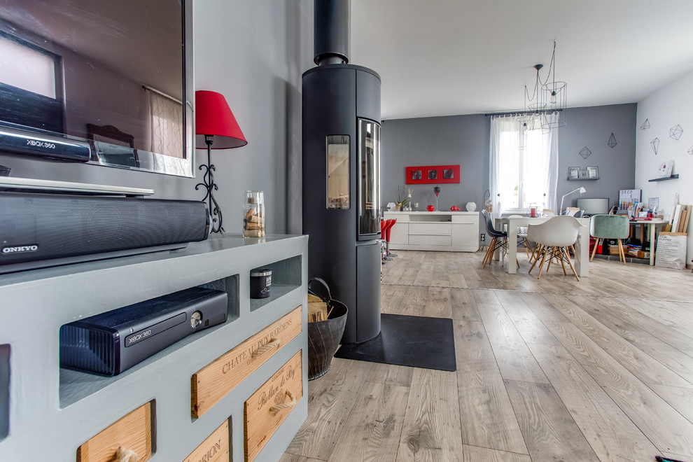 Cette image montre une grande salle de séjour design ouverte avec un mur gris, sol en stratifié, un poêle à bois, un téléviseur indépendant et un sol marron.