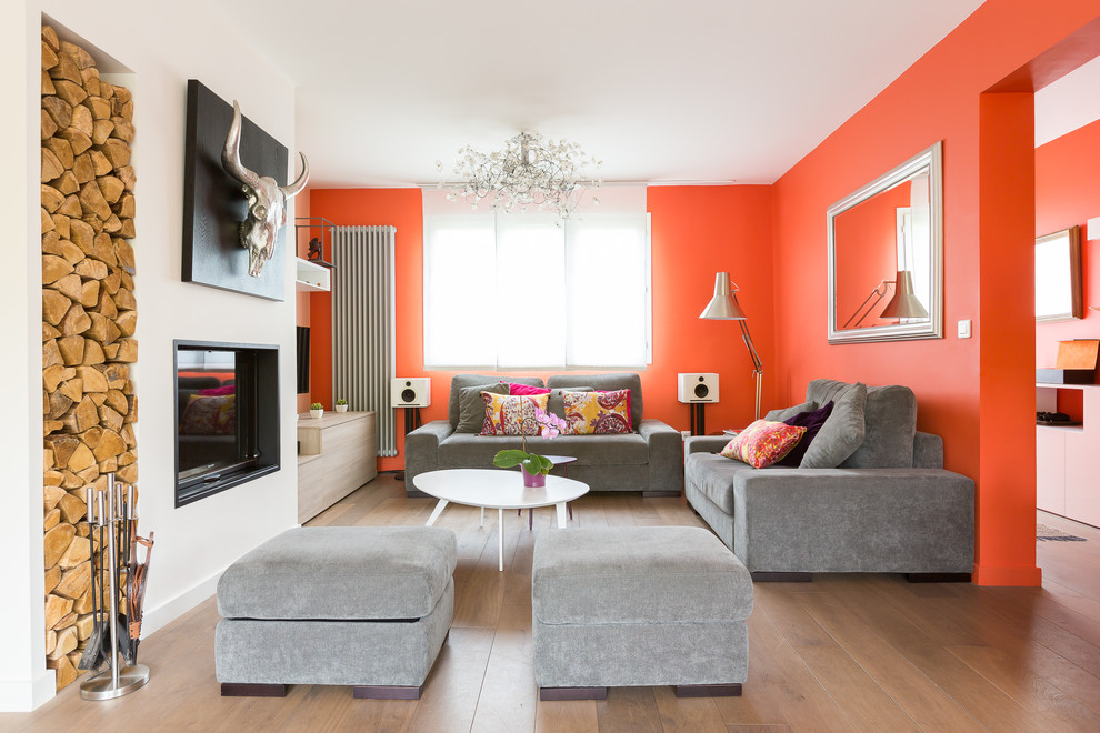 Imagen de sala de estar abierta actual grande con parades naranjas, suelo de madera en tonos medios, todas las chimeneas y televisor colgado en la pared