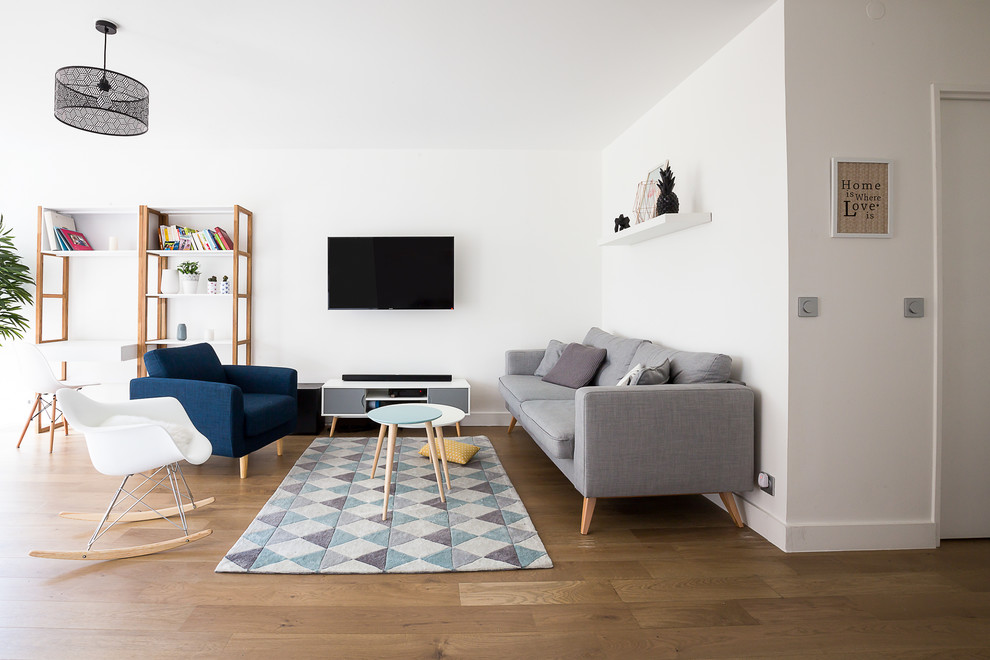 Example of a mid-sized danish open concept medium tone wood floor family room library design in Paris with white walls, no fireplace and a wall-mounted tv