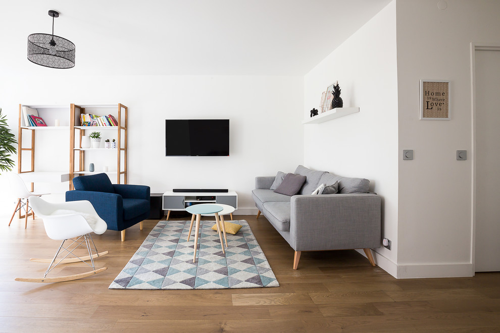 Imagen de sala de estar con biblioteca abierta escandinava de tamaño medio sin chimenea con paredes blancas, suelo de madera en tonos medios, televisor colgado en la pared y alfombra