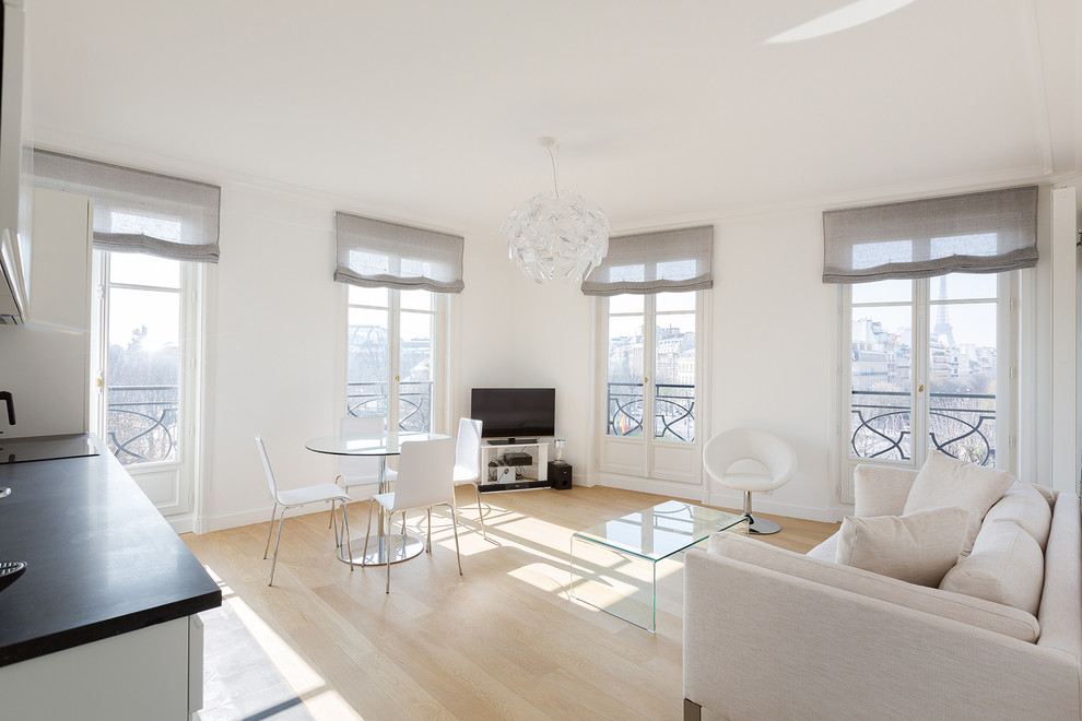 Imagen de sala de estar abierta actual de tamaño medio sin chimenea con paredes blancas, suelo de madera clara y televisor independiente