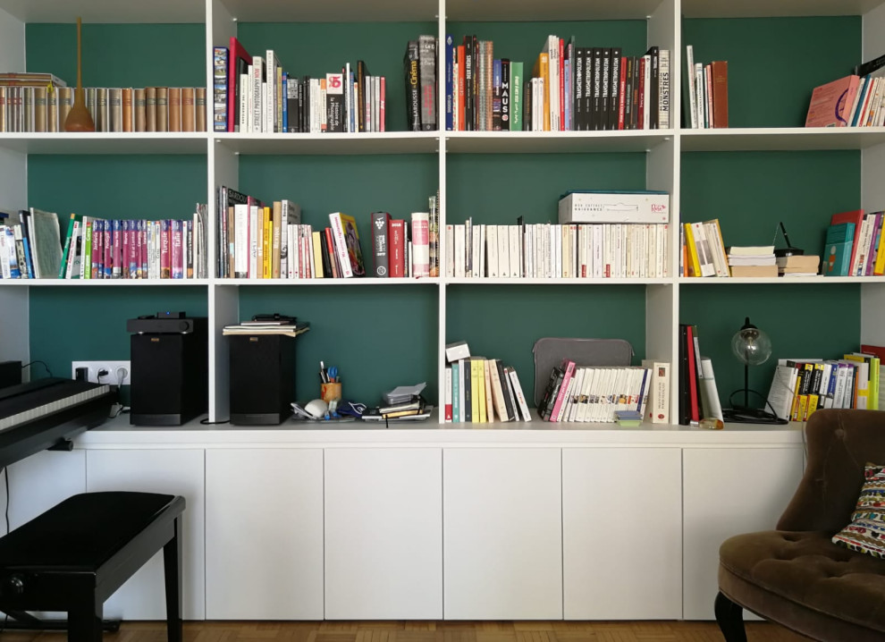 Immagine di un piccolo soggiorno design aperto con libreria, pareti verdi, parquet chiaro, nessun camino e pavimento marrone