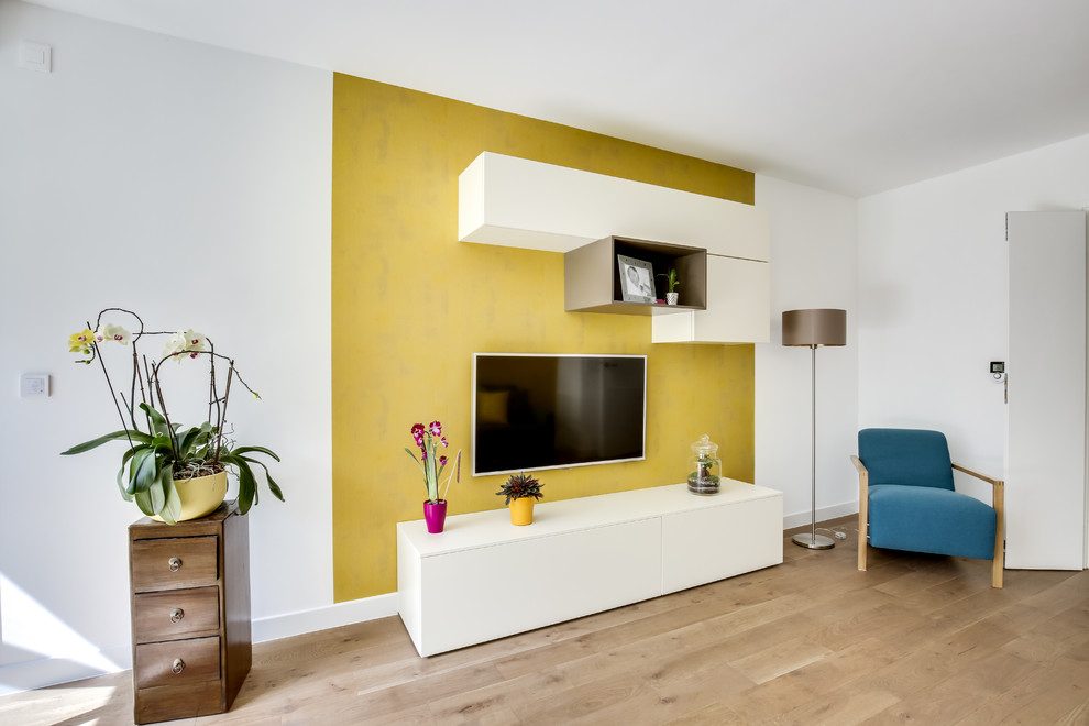 Réalisation d'une petite salle de séjour design ouverte avec un mur jaune, parquet clair, un téléviseur fixé au mur, un sol marron et aucune cheminée.