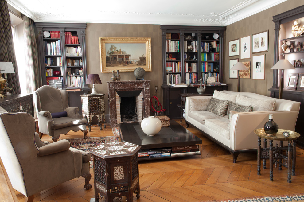 Immagine di un soggiorno eclettico con libreria, parquet chiaro, camino classico e pareti beige